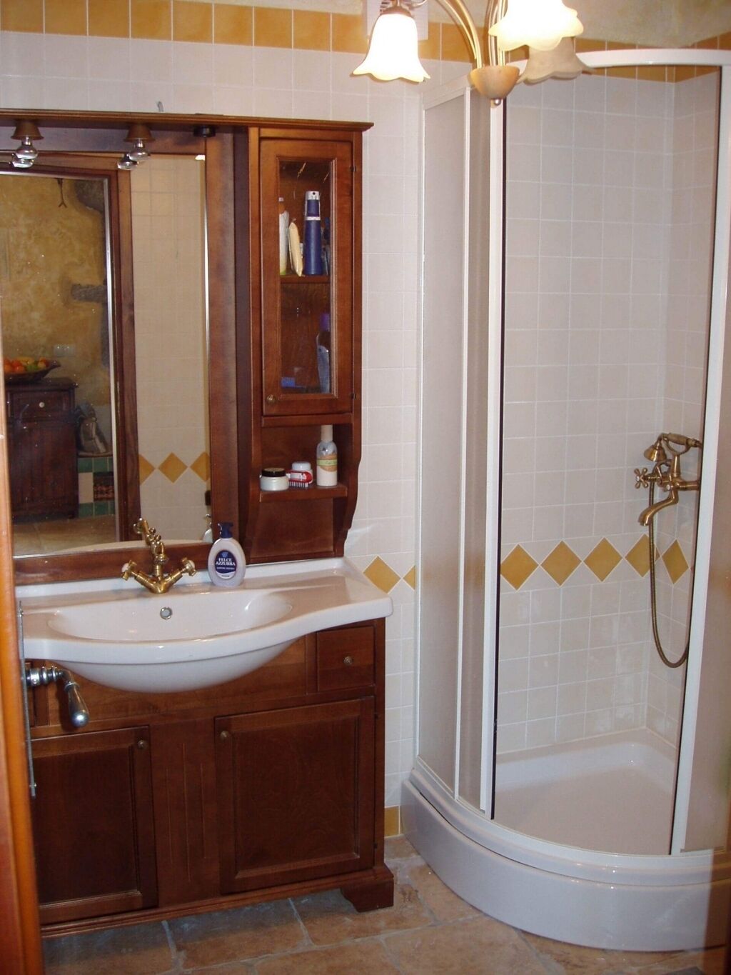 Een badkamer met een witte wastafel, houten kastjes, een spiegel en een douche met een glazen deur.