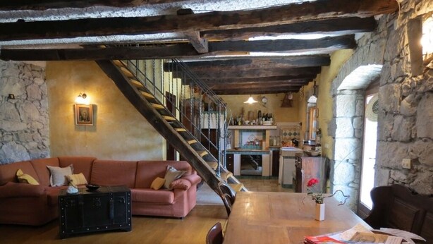 Un interior rústico con una mesa de comedor de madera, un sofá y una escalera que lleva a una zona de cocina.