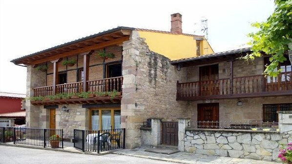 A two-story stone building with balconies, a yellow roof, and a stone wall.
