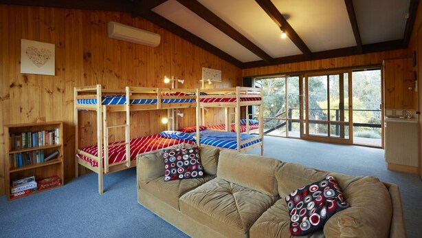 A cabin with bunk beds, a sofa, a bookshelf, and a view through large windows. - Edith's House (Fairhaven)