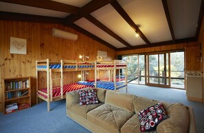 A cabin with bunk beds, a sofa, a bookshelf, and a view through large windows.