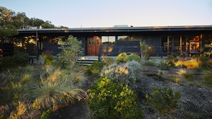 A modern house with a flat roof, large windows, and a wooden front door. - Edith's House (Fairhaven)