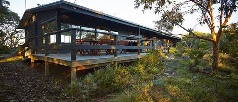 A modern two-story house with a deck, outdoor seating, and a barbecue grill.