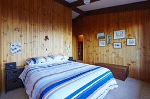 Ein Schlafzimmer mit einer holzverkleideten Wand, einem Bett mit gestreifter Bettdecke, einem Nachttisch und einem Beistelltisch.