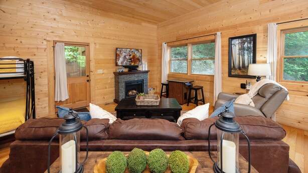 A cozy cabin interior with a fireplace, leather sofa, and a wooden dining table. - Private Cabin, FREE Pool Access, Putt Putt, Fishing, Tennis, Golf, Basketball (Sevierville)