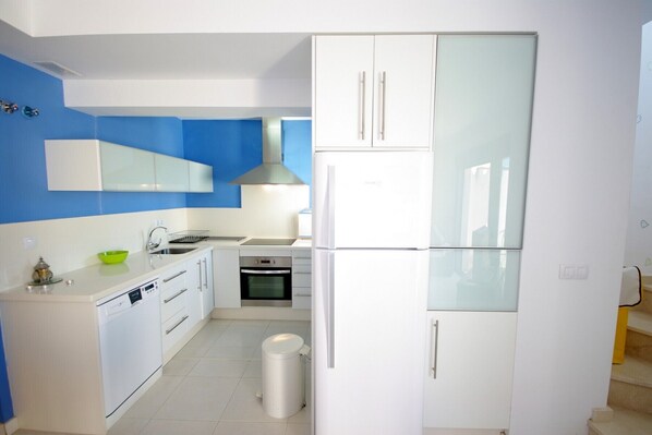 A modern kitchen with white cabinets, a stainless steel range hood, a built-in oven, and a dishwasher. - 92 - Apartamento Namasté (Tarifa)