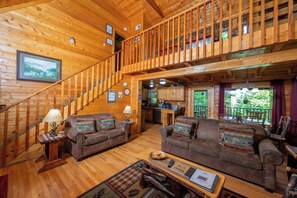 Ein Holzblockhaus-Interieur mit Treppe, zwei Sofas, einem Esstisch und einer Küchenzeile.