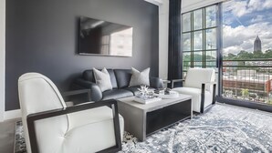 Ein modernes Wohnzimmer mit einer schwarzen Couch, weißen Sesseln, einem Couchtisch und einem großen Fenster mit Blick auf die Stadt.