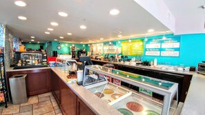 A brightly lit ice cream shop with a teal wall, a counter displaying various ice cream flavors, and a glass display case with ice cream cones.