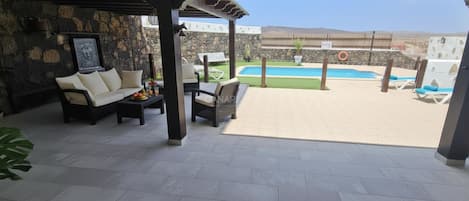 Eine Außenpatio mit einer Couch, Stühlen, einem Tisch, einem Pool und einer Steinmauer.