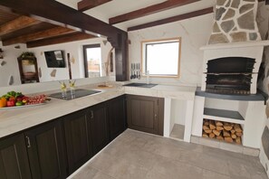 A kitchen with dark cabinets, a marble countertop, a stone fireplace, and a window.