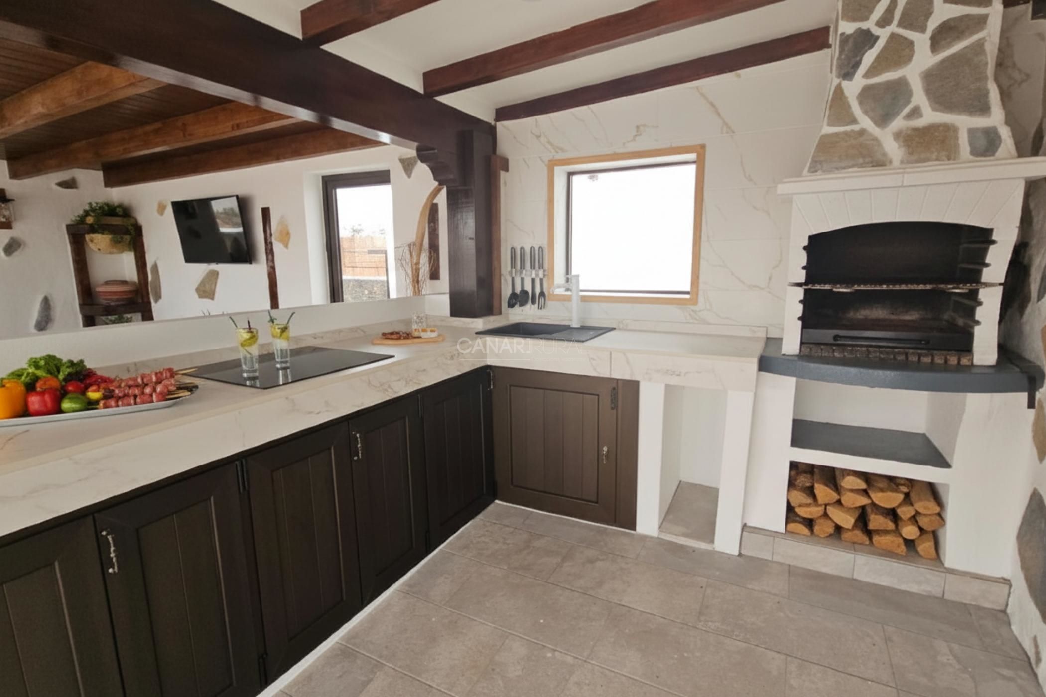 A kitchen with dark cabinets, a marble countertop, a stone fireplace, and a window.