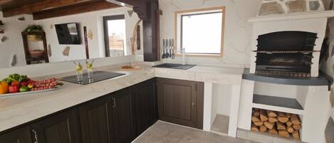 A kitchen with dark cabinets, a marble countertop, a stone fireplace, and a window.