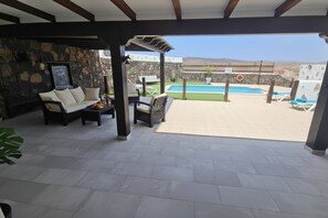An outdoor patio with a sofa, chairs, and a table, a pool, and a stone wall.