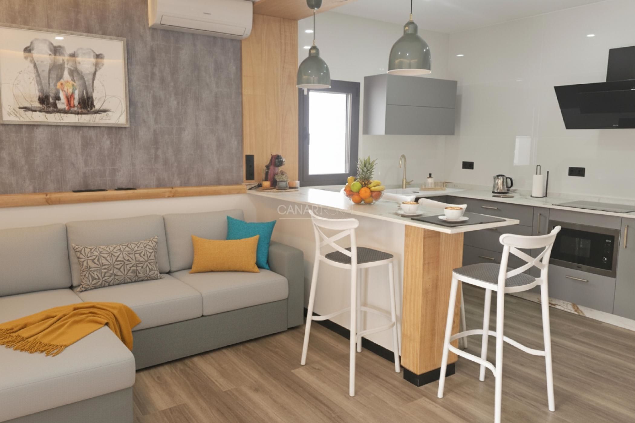 Una cocina moderna con una isla central, taburetes blancos y un sofá gris con cojines estampados.