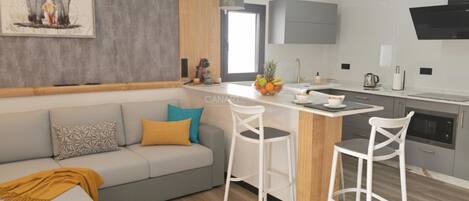 Una cocina moderna con una isla central, taburetes blancos y un sofá gris con cojines estampados.