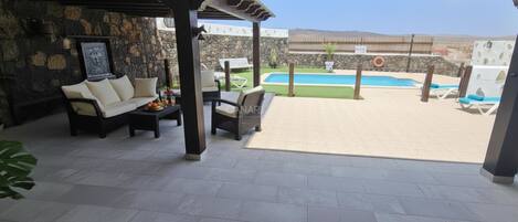 Una terrazza esterna con un divano, sedie, un tavolo, una piscina e un muro in pietra.