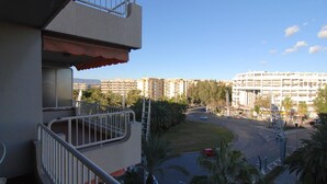 Un balcone con vista su un edificio a più piani, una strada con auto e palme.