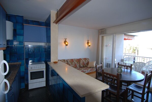 Una cocina compacta con baldosas azules, una estufa blanca y un pequeño comedor con una mesa y sillas de madera.