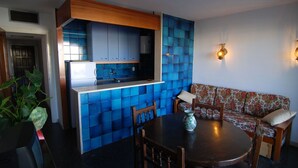 Una cucina compatta con piastrelle blu, un piano di lavoro in legno e un lavello incassato. C'è un'area pranzo con un tavolo rotondo e sedie, e un divano con rivestimento floreale.