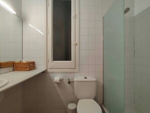 A bathroom with a toilet, a sink, a window, and a shower.