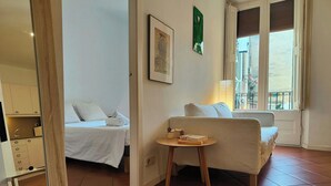 Un cuarto de hotel con cama, un sofá, una pequeña mesa con libros, una ventana con vista y un adorno verde en la pared.