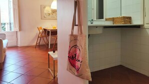 Una habitación con comedor, una pared blanca con un cuadro enmarcado, una lámpara colgante y un baño con espejo y estante.
