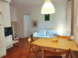 A dining area with a table, chairs, a sofa, a television, and a wall-mounted lamp.