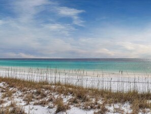 Una playa con agua turquesa cristalina, arena blanca y vegetación escasa.