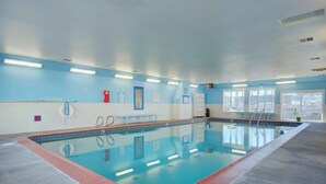 An indoor swimming pool with clear blue water, a tiled deck, and a view of the city through large windows.