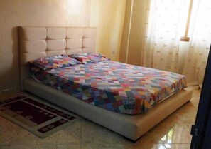 A bed with a quilt, a headboard, and a rug.