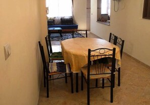 A dining area with a round table and six chairs, a blue sofa with cushions, and a window with curtains.