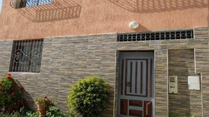 Un bâtiment doté d’une façade à motifs, d’une entrée fermée par un portail et d’un petit jardin agrémenté de fleurs rouges.