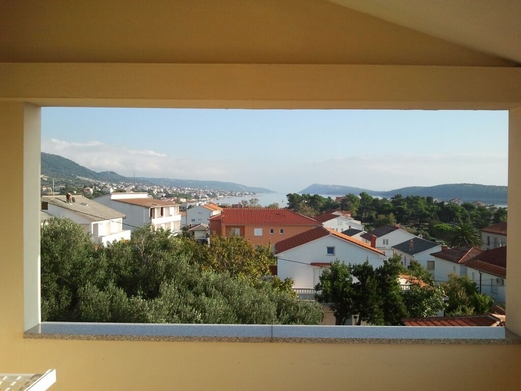 A view from a window overlooking a residential area with houses, trees, and distant hills.
