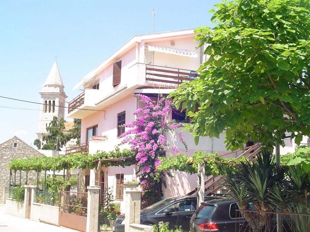 Un edificio de dos plantas con un balcón, una torre de piedra y un coche estacionado adelante.
