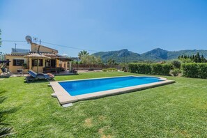 Una casa con piscina, patio con poltrone relax e vista sulle montagne.