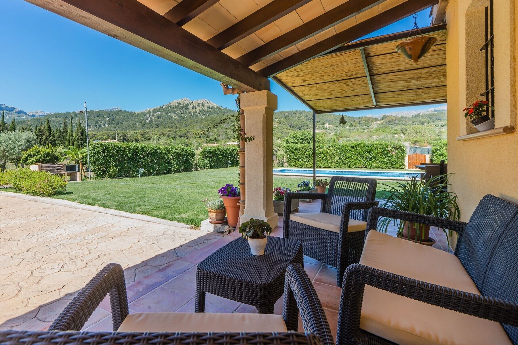Eine überdachte Terrasse mit Korbmöbeln und Blick auf Pool und Grünflächen.