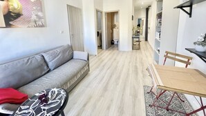 A modern living room with a grey sofa, a small table, and a dining area with a wooden chair.
