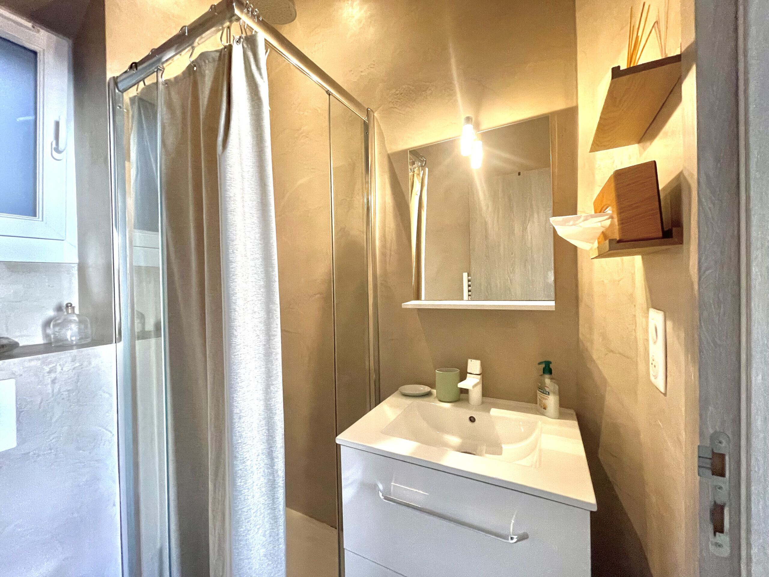 Une salle de bain équipée d’une douche, d’un lavabo, d’un miroir et d’une étagère où sont rangés les articles de toilette.
