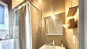 A bathroom with a shower, a sink, a mirror, and a shelf with toiletries.