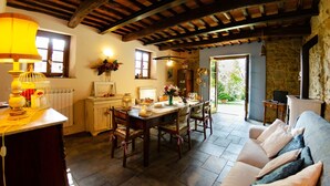 A rustic kitchen with wooden beams, a dining table with chairs, a sofa, and a stone wall.
