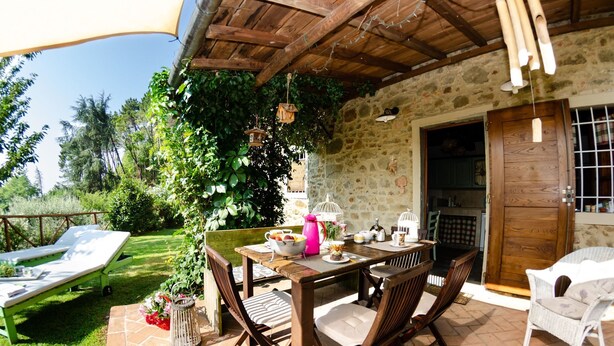 An outdoor patio with a wooden table set for dining, surrounded by wicker chairs.