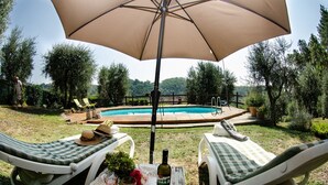 A poolside setting with two lounge chairs, a table with a bottle and glasses, and a large umbrella providing shade.