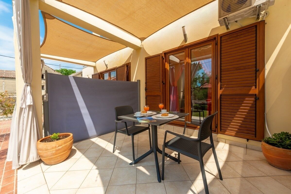 A patio with a table set for two, featuring a small potted plant and a table with a plate of food and drinks.