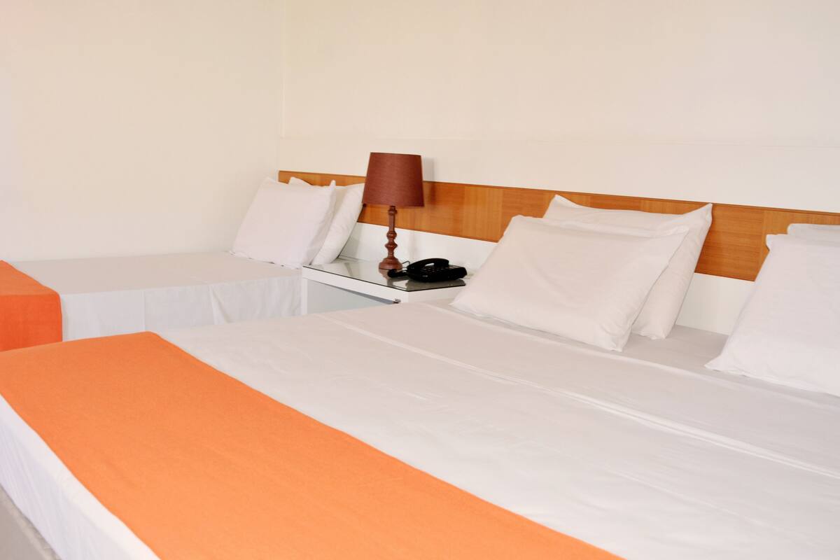 Quarto de hotel com duas camas, mesa de cabeceira, abajur e telefone.