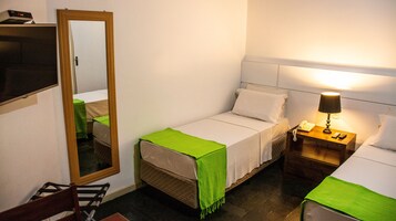 Una habitación pequeña y limpia con una cama, una mesita de noche con lámpara, un espejo y una silla.