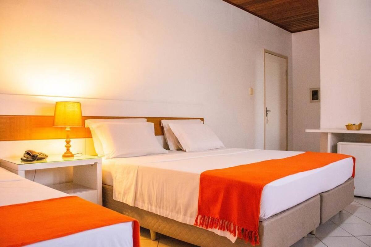 Quarto de hotel com cama, mesa de cabeceira, luminária e uma pequena mesa com uma tigela.