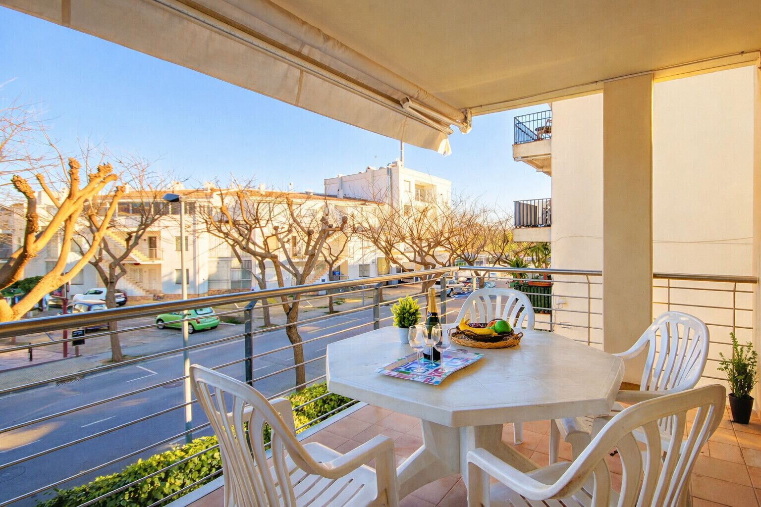 A balcony with a table, chairs, a bottle, a glass, and a basket of fruit.