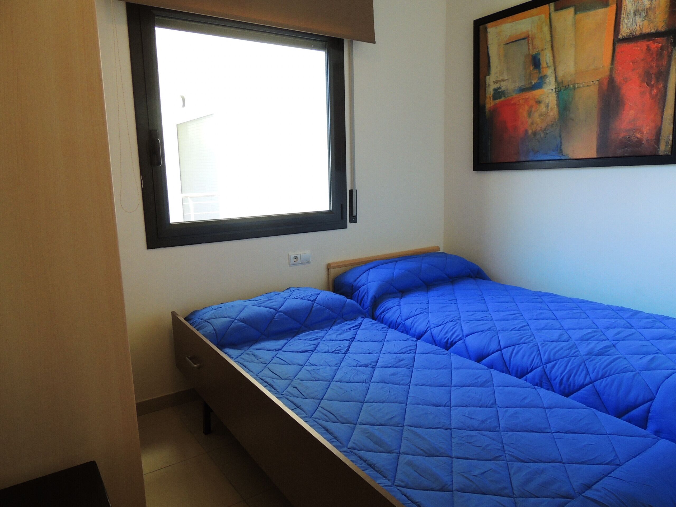 Een kleine slaapkamer met een enkel bed, een raam en een schilderij aan de muur.