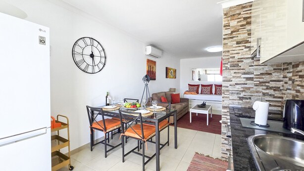 A modern kitchen with a dining area, a clock, and a stone backsplash. - Apartment Praia Rocha Sea View Sunshine (Portimão)